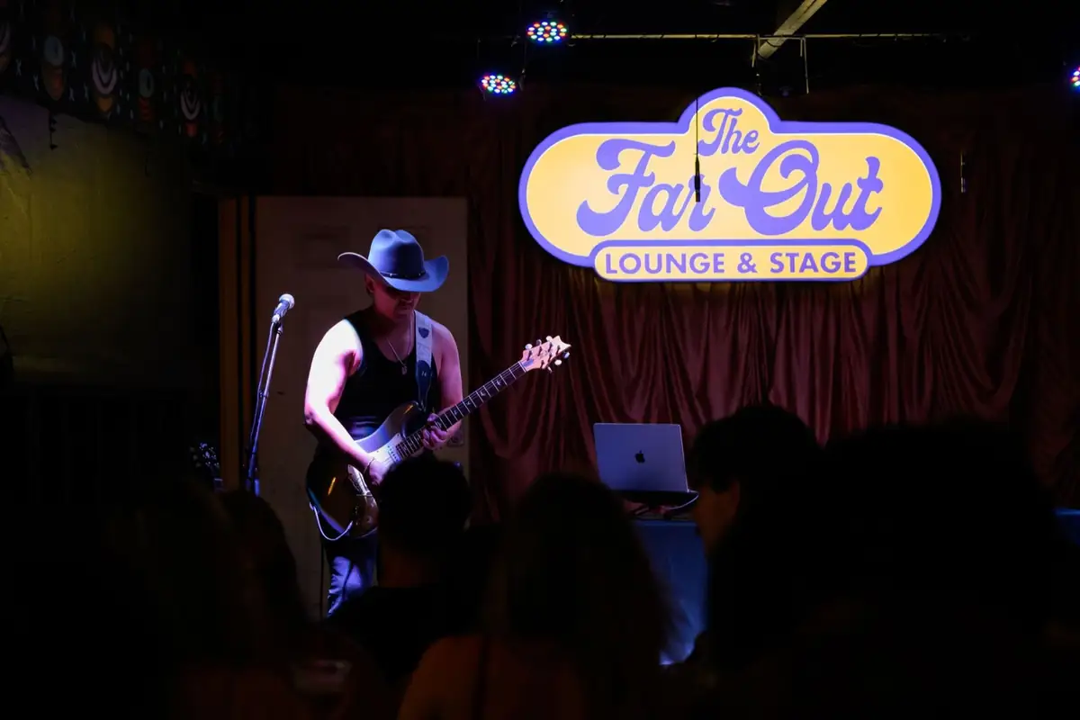 Kristian Cruz on guitar under The Far Out Lounge sign in Austin