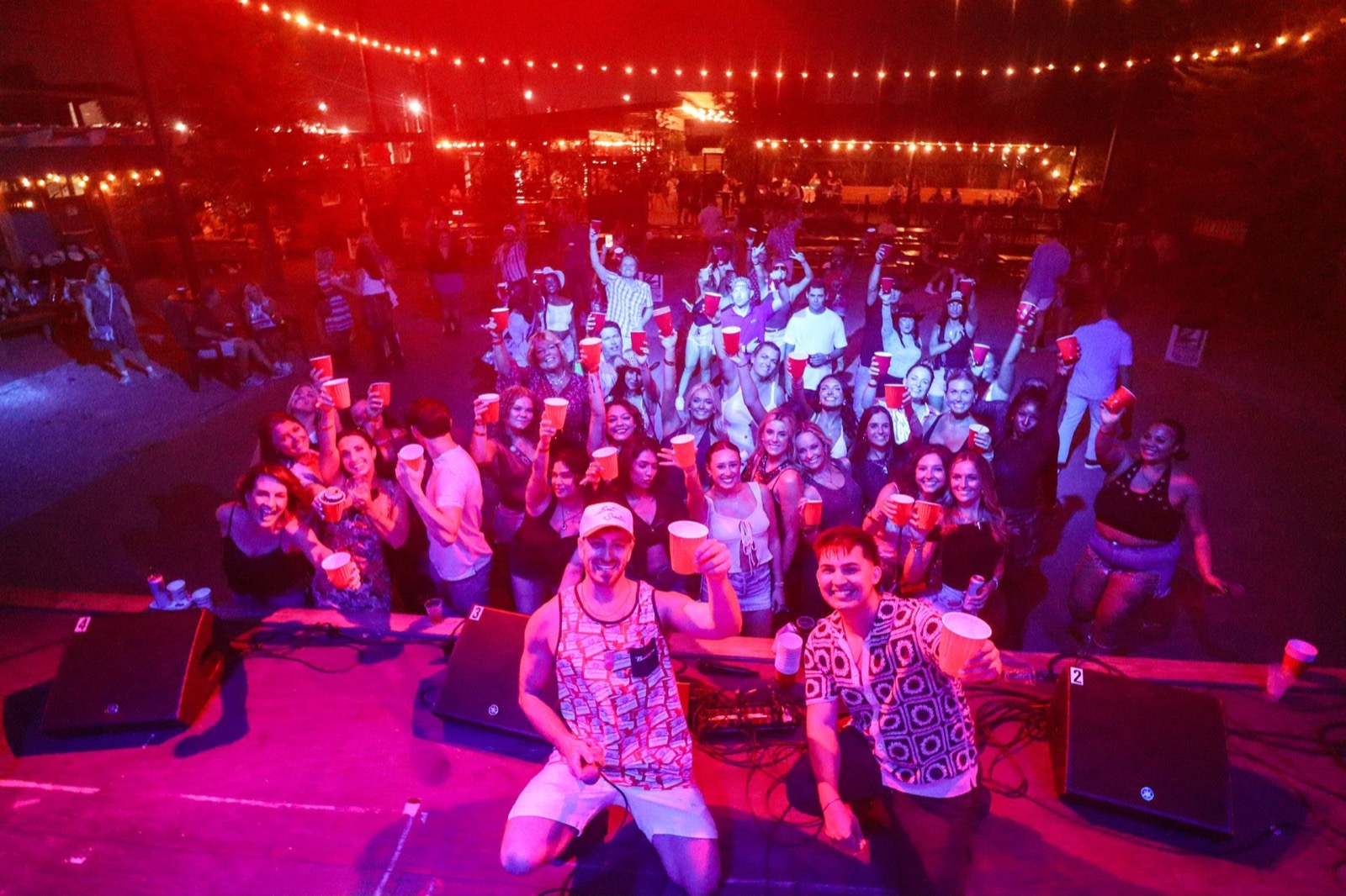 Jordan Miller and Kristian Cruz with the whole Broadside crowd raising cups under the string lights, New Orleans