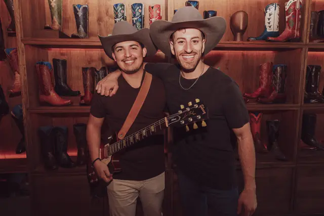 Kristian Cruz with his guitar and Jordan Miller in front of the Lucchese boot wall