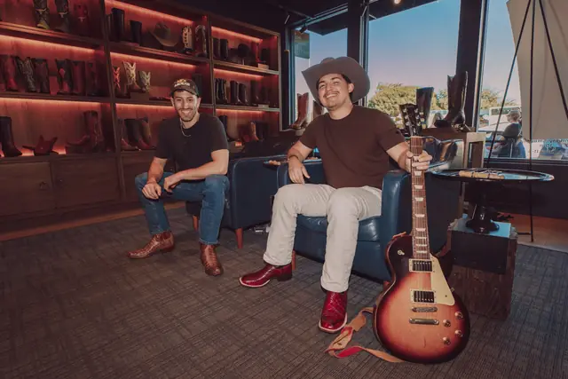 Jordan Miller and Kristian Cruz seated with a guitar inside Lucchese