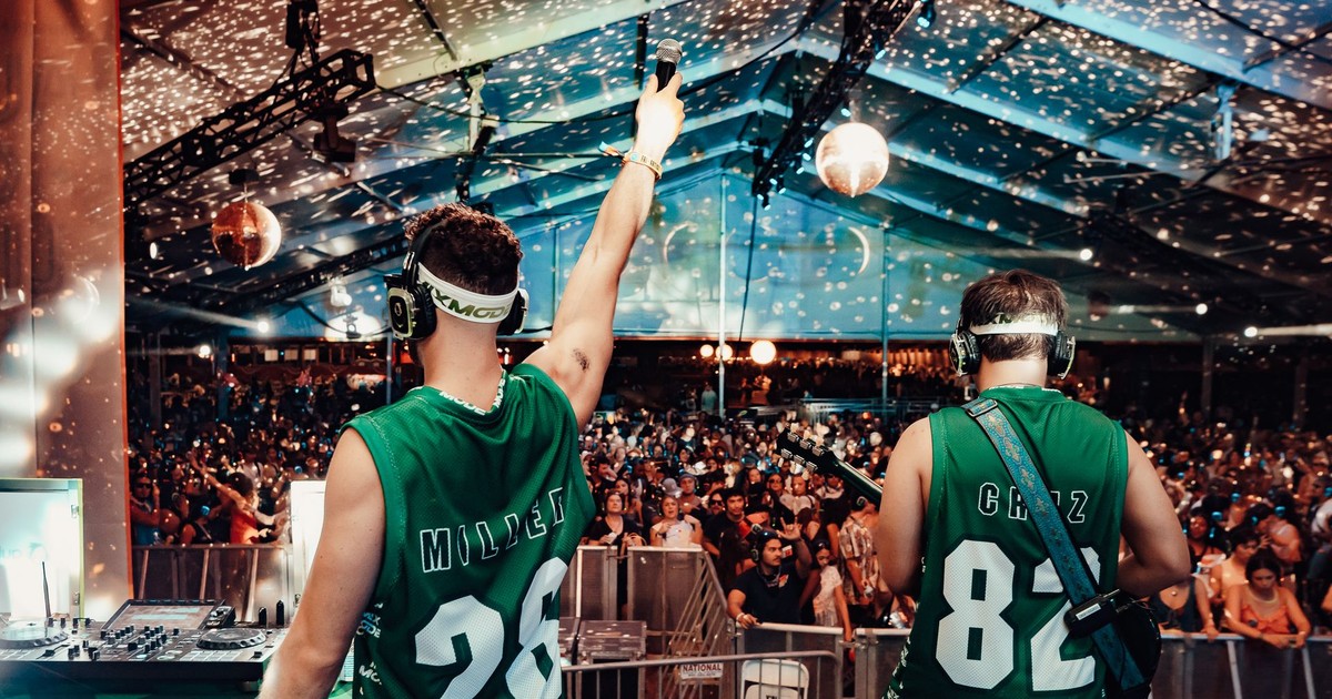 Jordan Miller and Kristian Cruz of MIXMODE, seen from behind in green jerseys, facing a silent disco crowd under a tent at ACL Fest 2026.